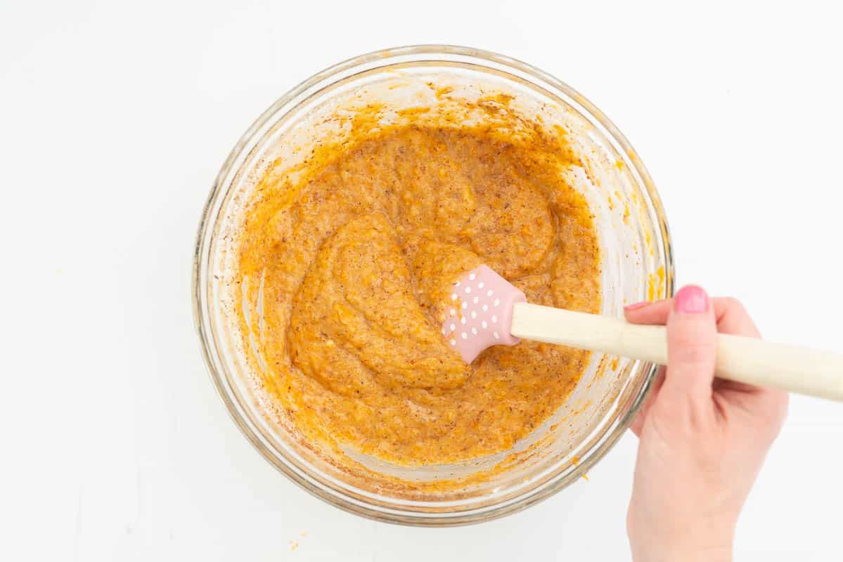 Sweet potato muffin batter being folded together with a spatula.