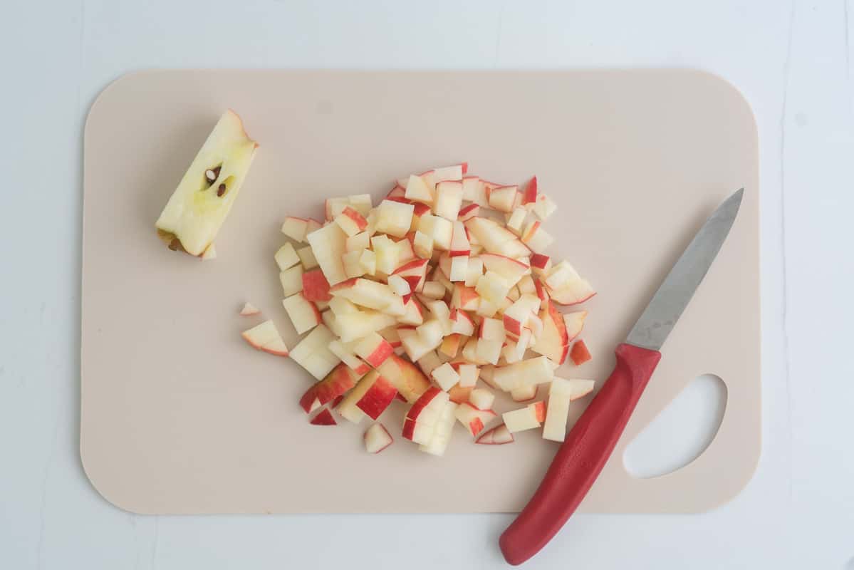 A chopping board covered in diced apple with a small red handled fruit knife.