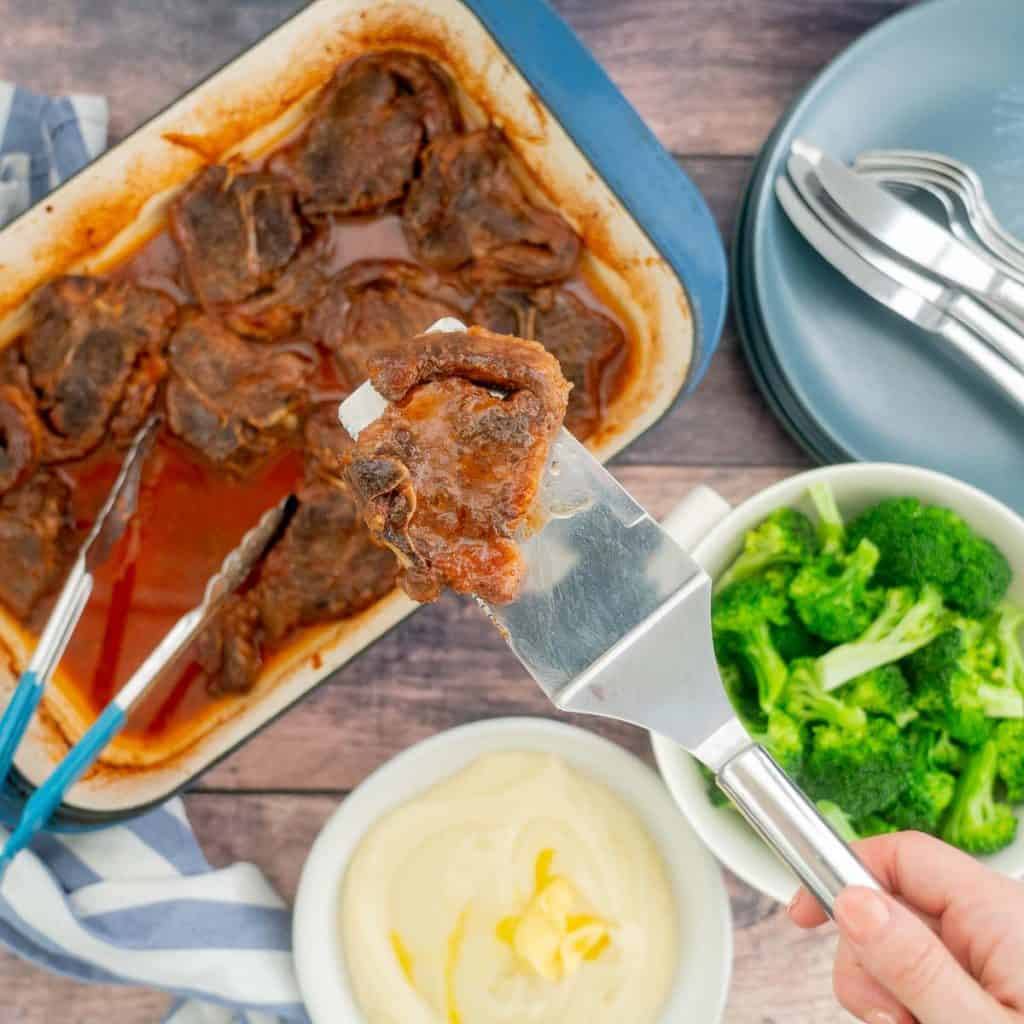 A marinaded lamb chop on a spatula being held above a family dinner table.
