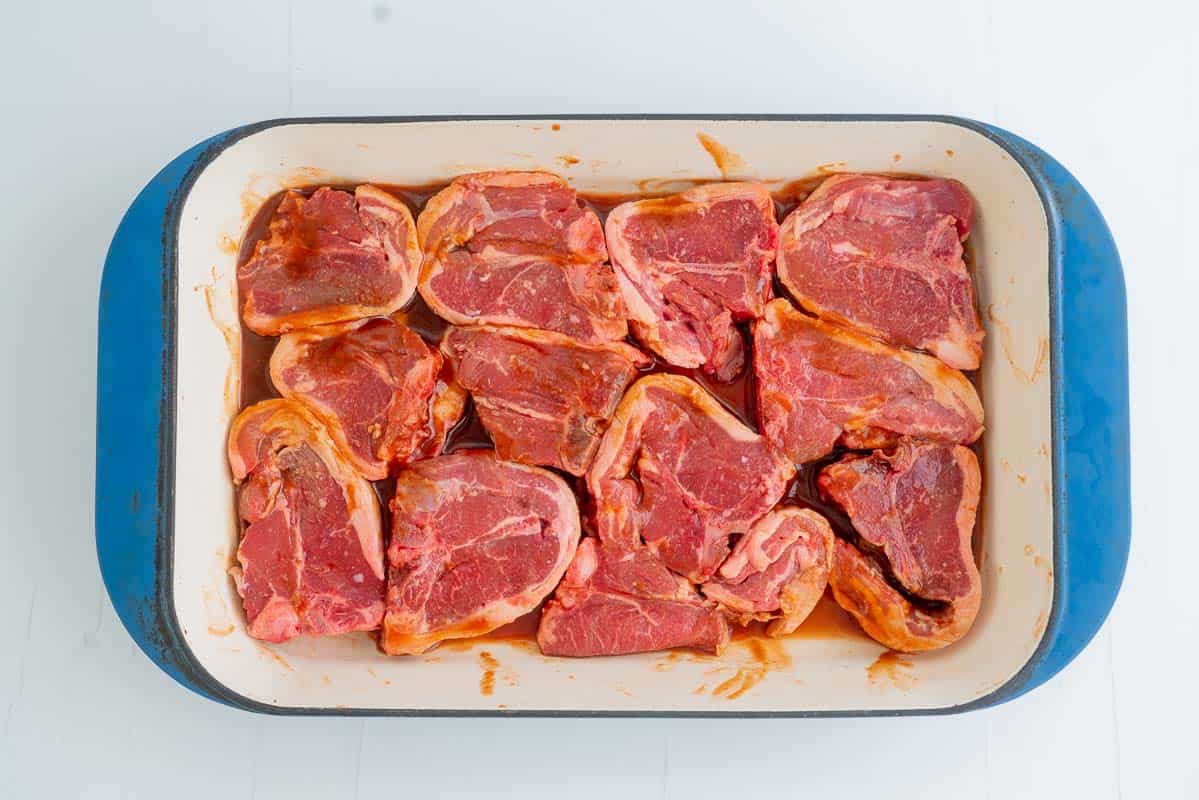 12 lamb loin chops covered in marinade in a blue ceramic baking dish.