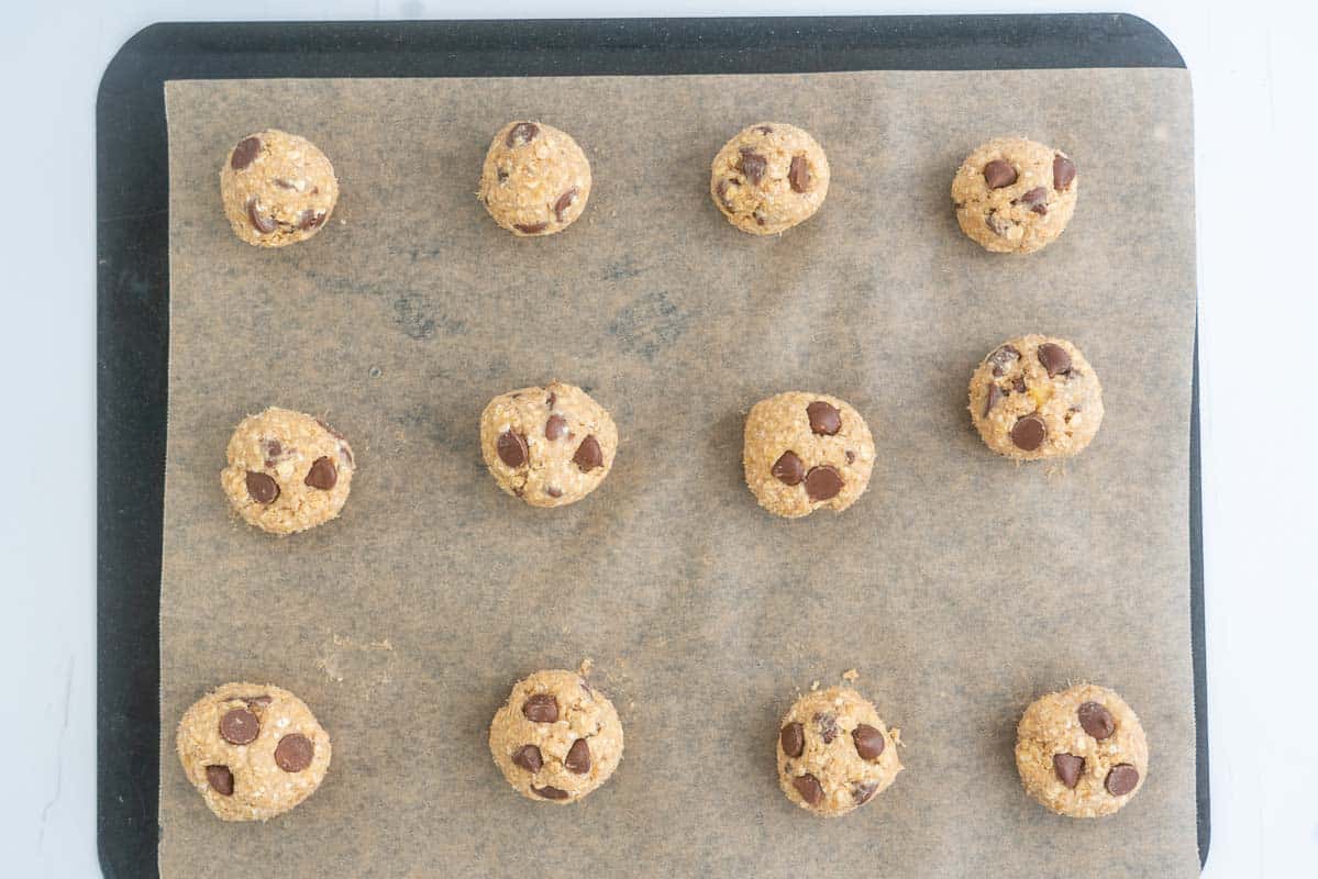 12 balls of choc chip oatmeal cookie dough on a lined baking tray.