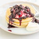 A short stack of pancakes drizzled with blueberry compote and yoghurt.