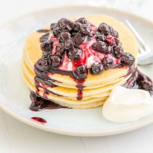 A short stack of pancakes drizzled with blueberry compote and yoghurt.