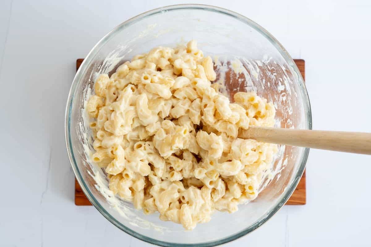 A large glass bowl of cooked macaroni elbows covered in a thick white sauce.