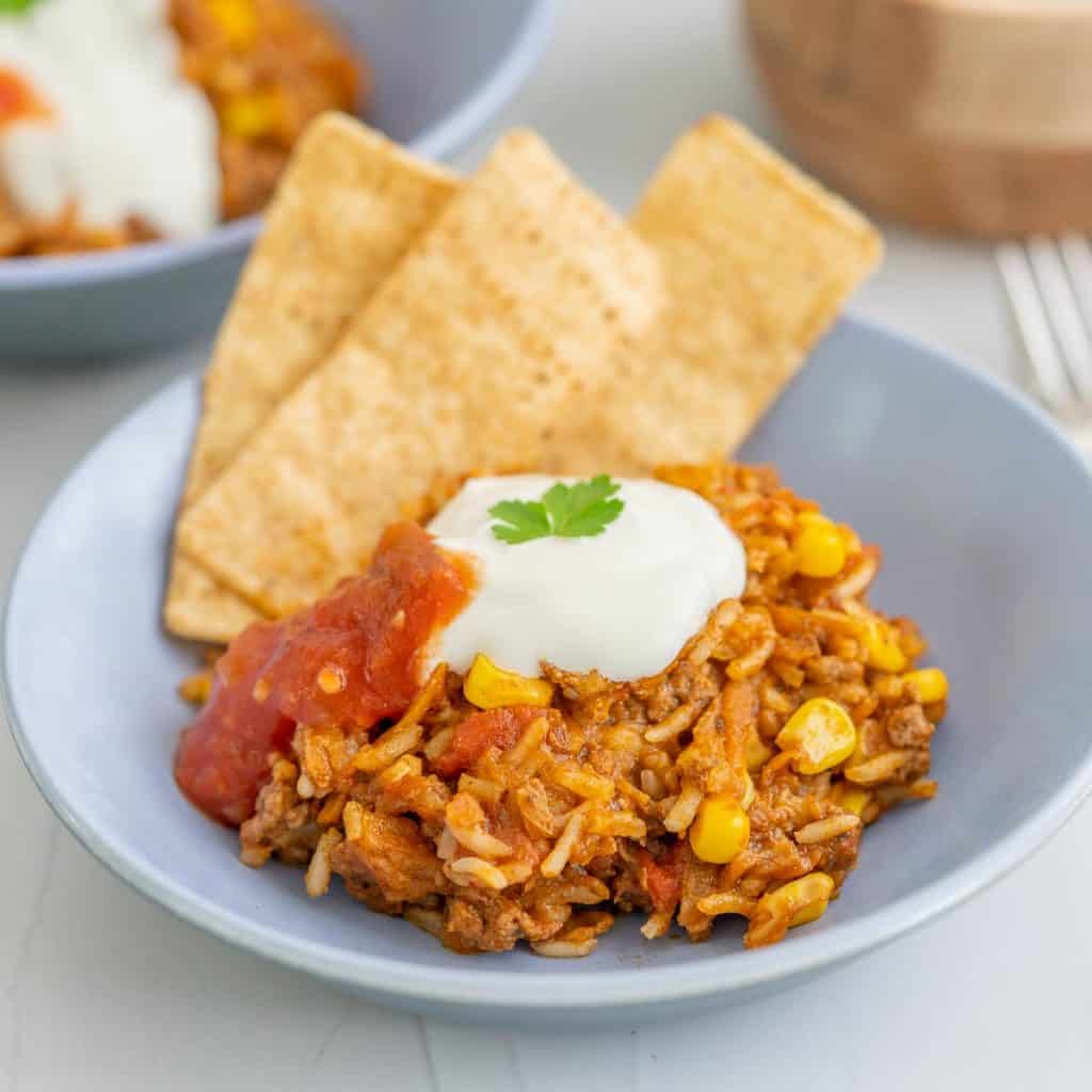 A bowl of mince and rice, garnished with sour cream, coriander and tortilla chips.