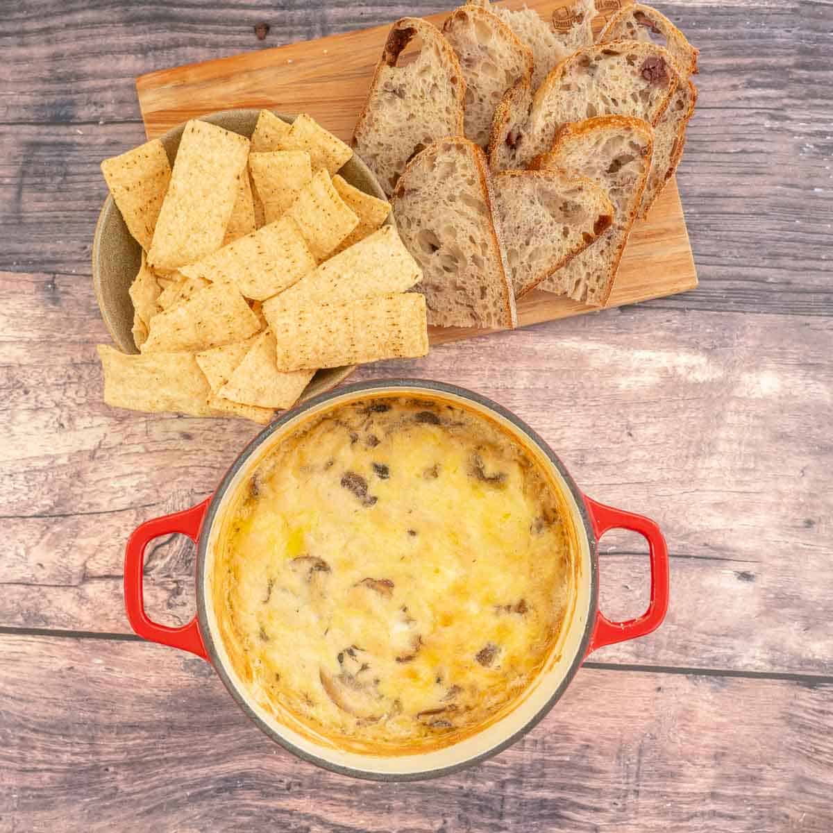 A baked cheese dip with a wooden board of chips and crusty bread.