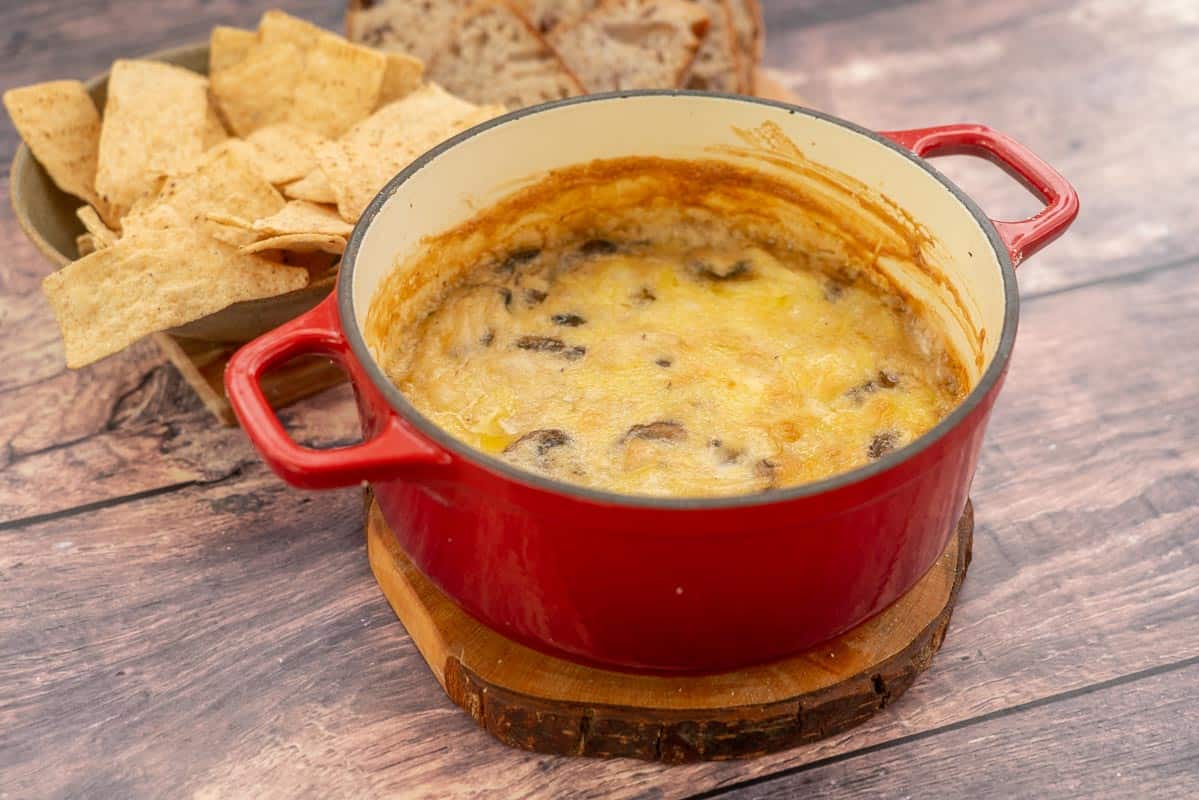 A warm cheese dip in a red ceramic baking dish ready to be served.