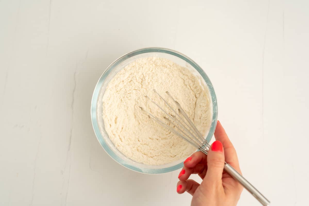 A glass mixing bowl of flour and a whisk.