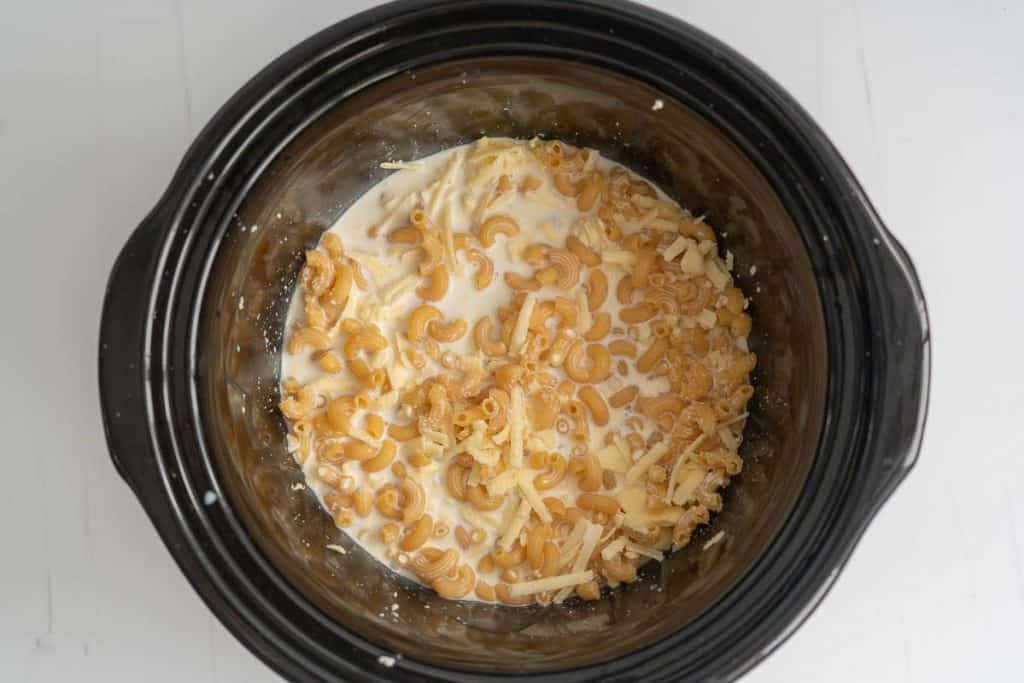 Dry elbow pasta, grated cheese and milk mixed together in a large black dish.