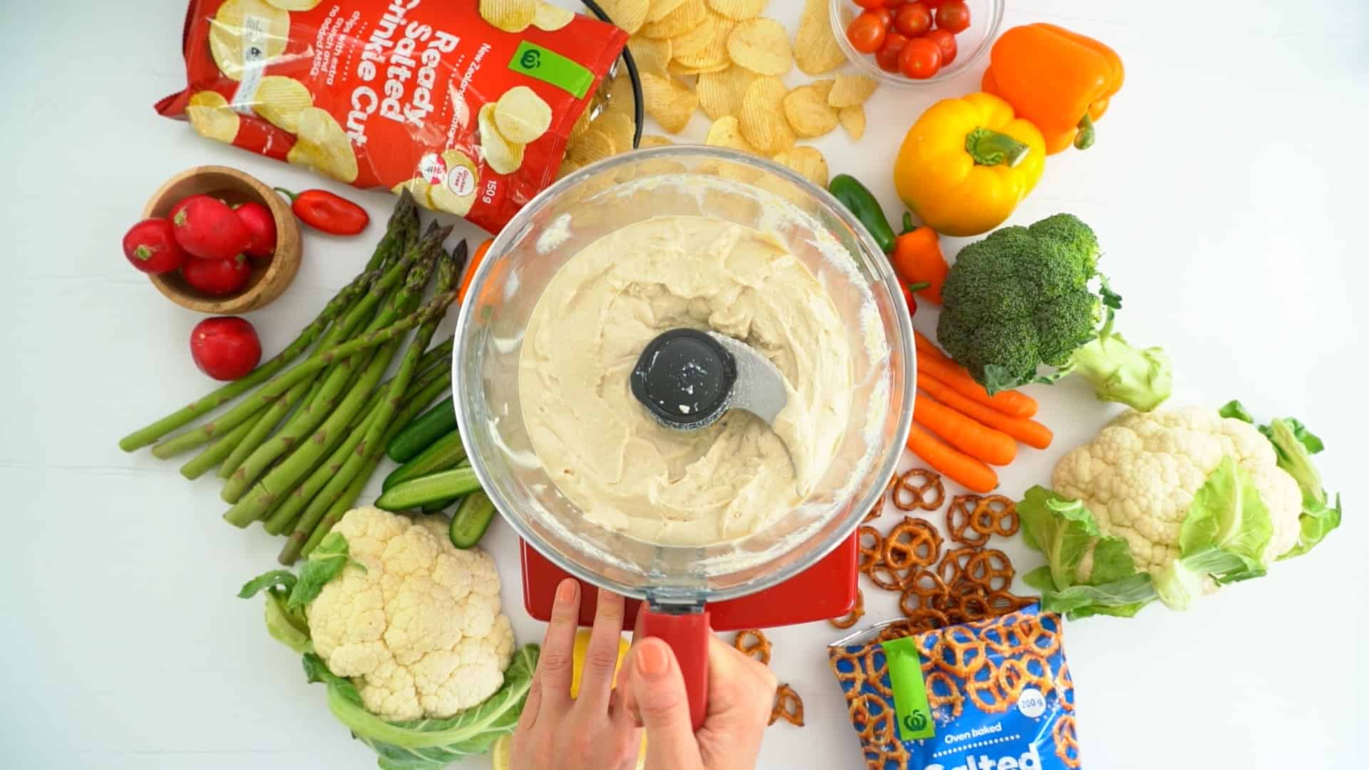 Vegan onion dip in a food processor surrounded by colourful fresh produce.