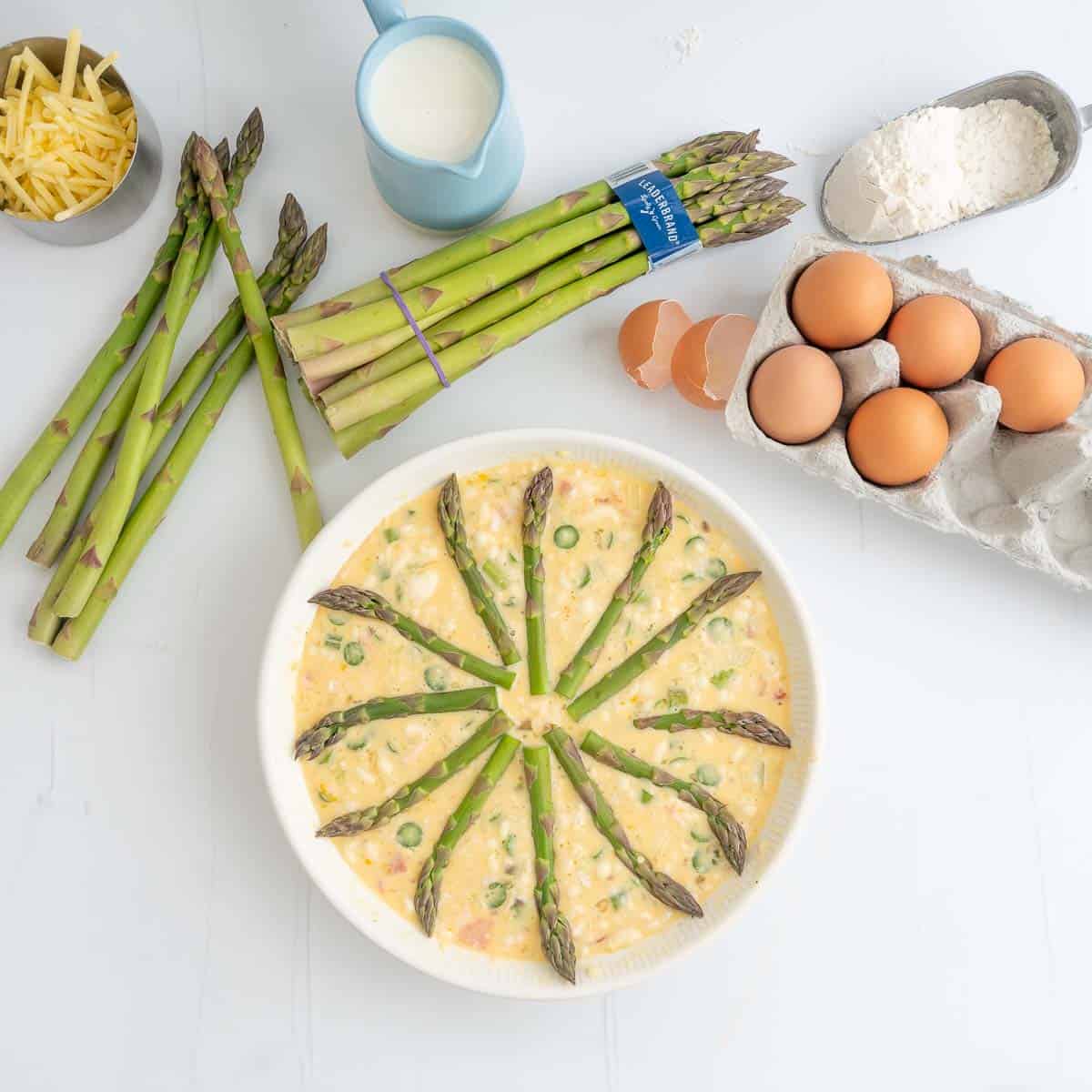 Uncooked quiche topped with asparagus spears like a clock face.