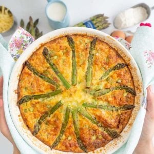 A quiche topped with asparagus being held above a bench top.