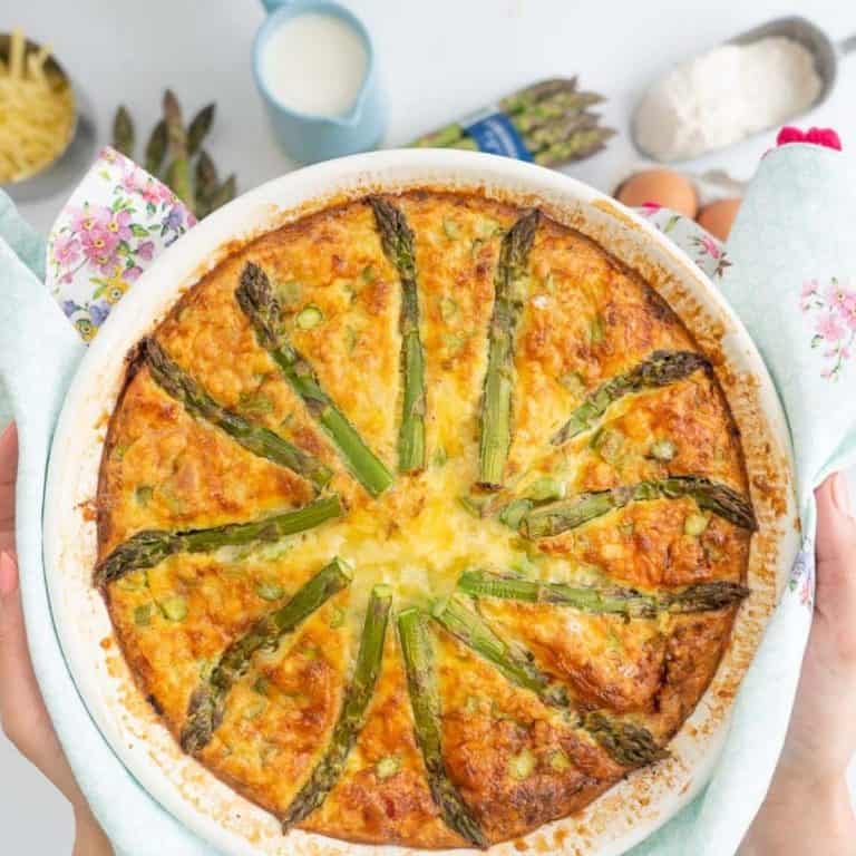 A quiche topped with asparagus being held above a bench top.