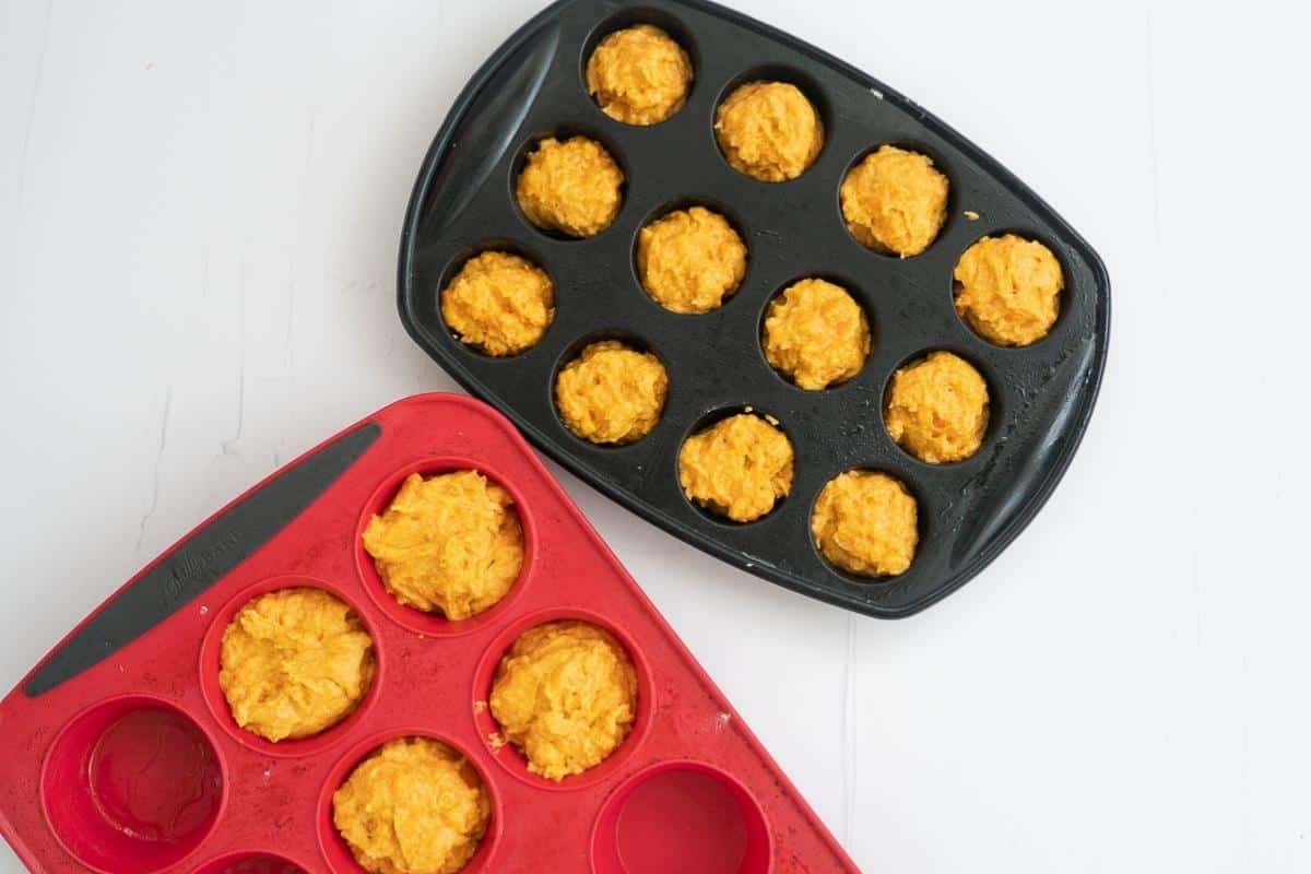 Carrot muffin batter portioned into a nb;lack mini muffin tray and a red standard muffin tray/