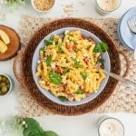 A large bowl filled with pasta, salami, sundried tomatoes, feta and spinach leaves.