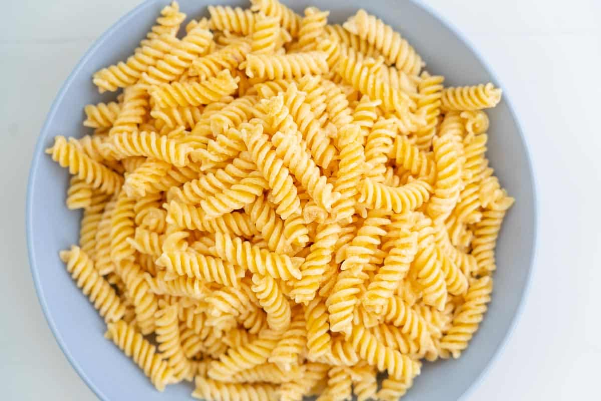 Pasta dressed with a sun dried tomato dressing in a large blue ceramic bowl.