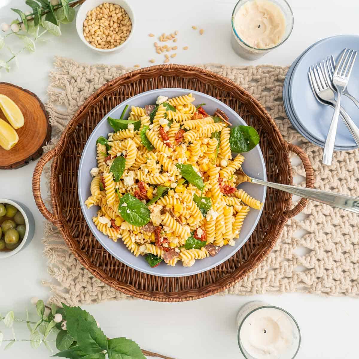 A large bowl of pasta salad resting on a wicker serving tray on a family dinner table.
