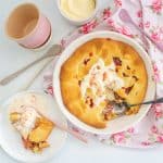 A rhubarb pie in a white pie dish, topped with a scoop of melted ice cream.