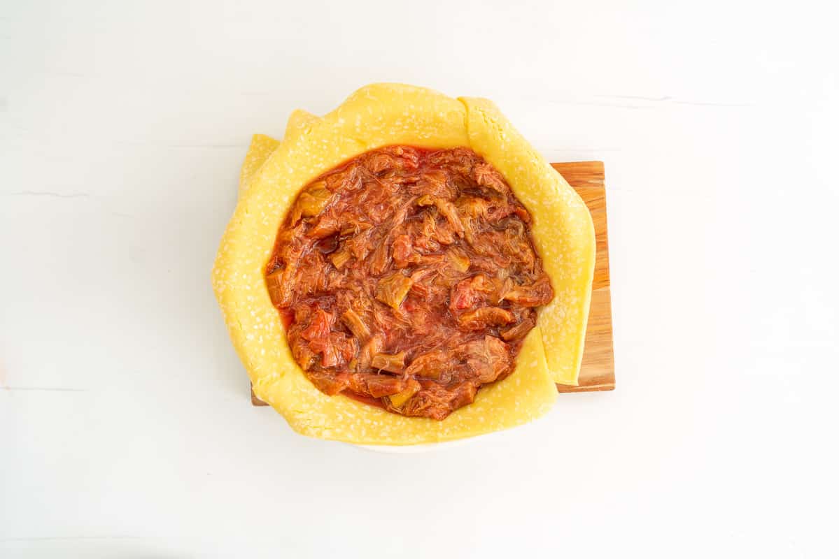 A pie dish lined with pastry filled with rhubarb filling.