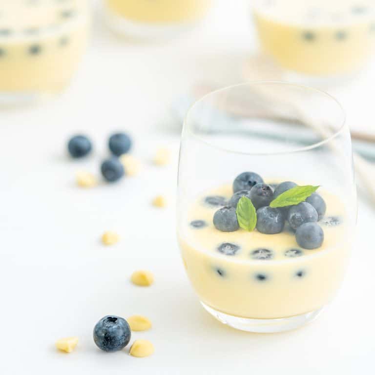 A glass filled with white chocolate mousse garnished with fresh blueberries and mint leaves.