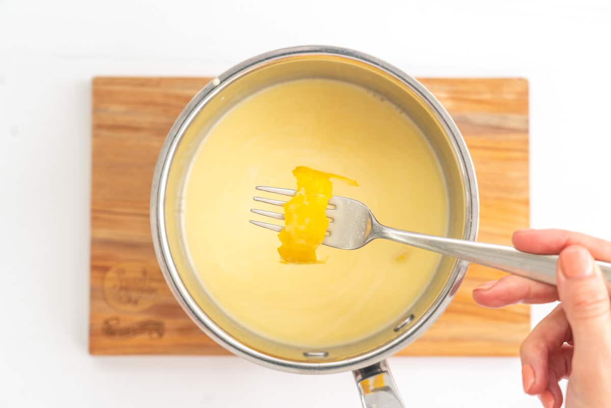 Strip of lemon zest being fished out of a saucepan of cream with a fork.