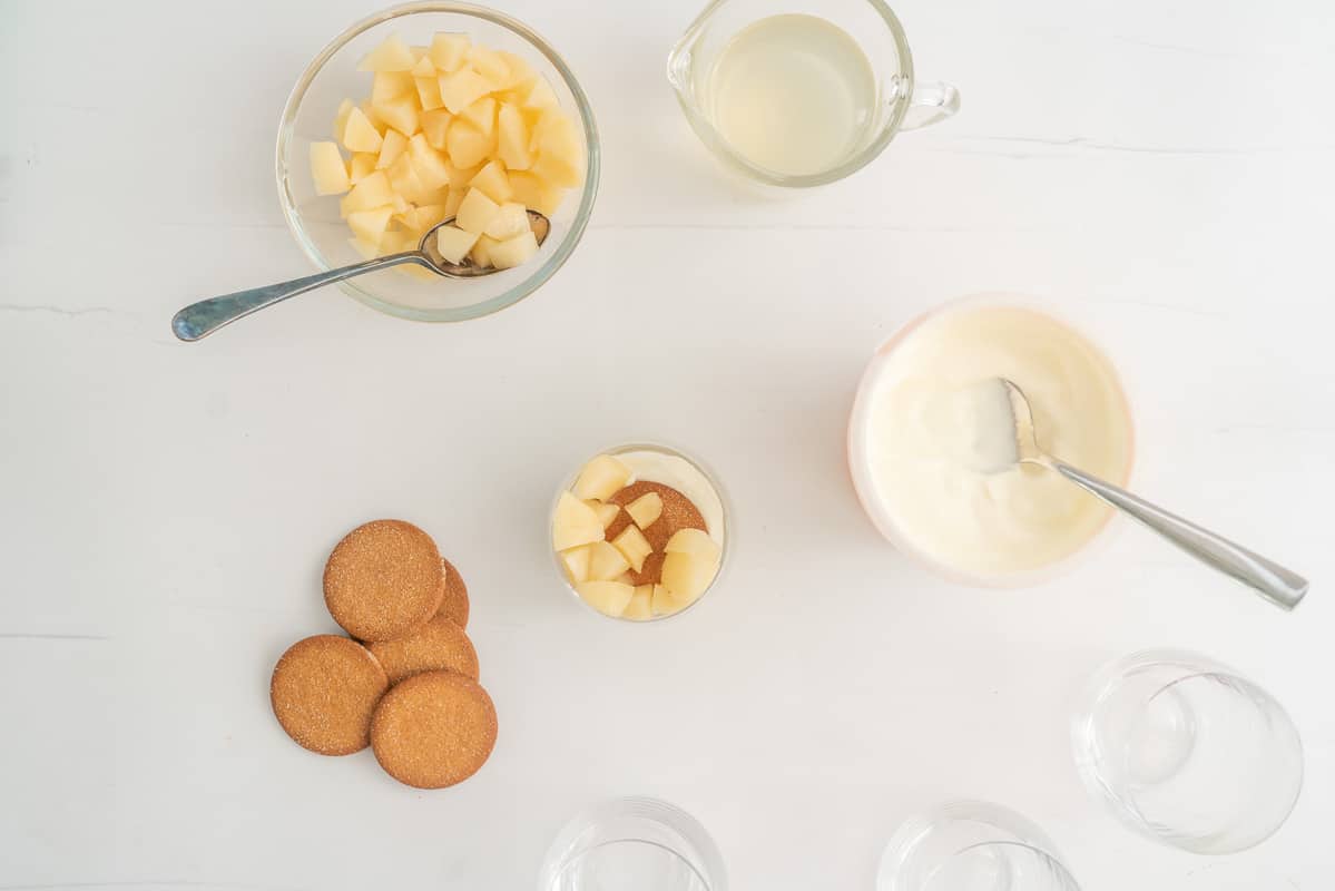A glass with cubes of pears, gingernut biscuit and yogurt in the bottom, surrounded by more pears, cookies and yogurt.