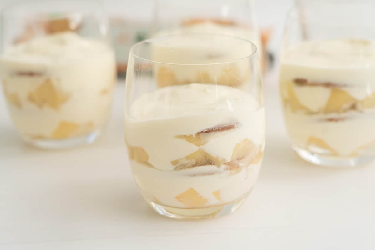 four glases filled with layers of pears, cookies, and yoghurt.
