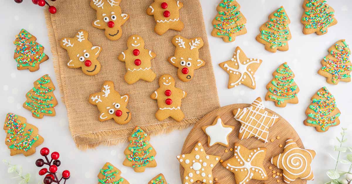 A selection of decorated gingerbread cookies laid out on a counter top, shapes include stars, reindeer, gingerbread men and Christmas trees.