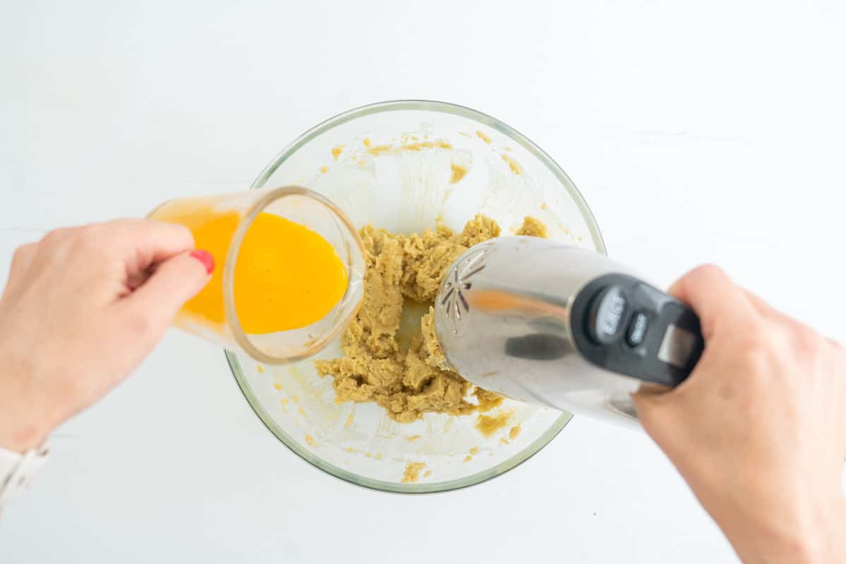 An electric beater beating in whisked eggs to creamed butter and sugar.