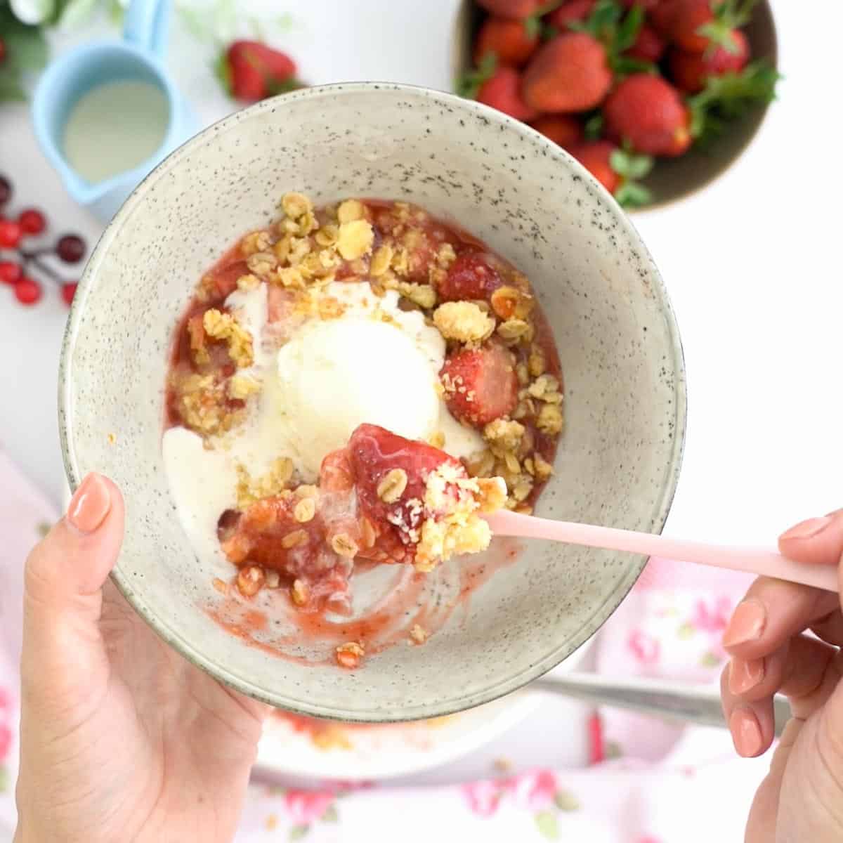 A bowl full of stewed strawberries and crumble topping with vanilla ice cream.