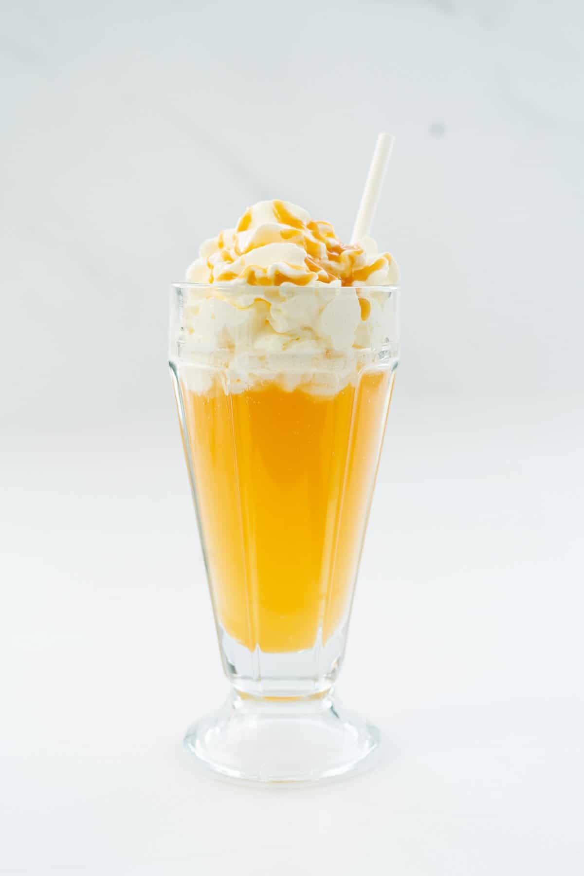 Golden butterbeer topped with whipped cream and caramel sauce in a tall ice cream sundae glass.