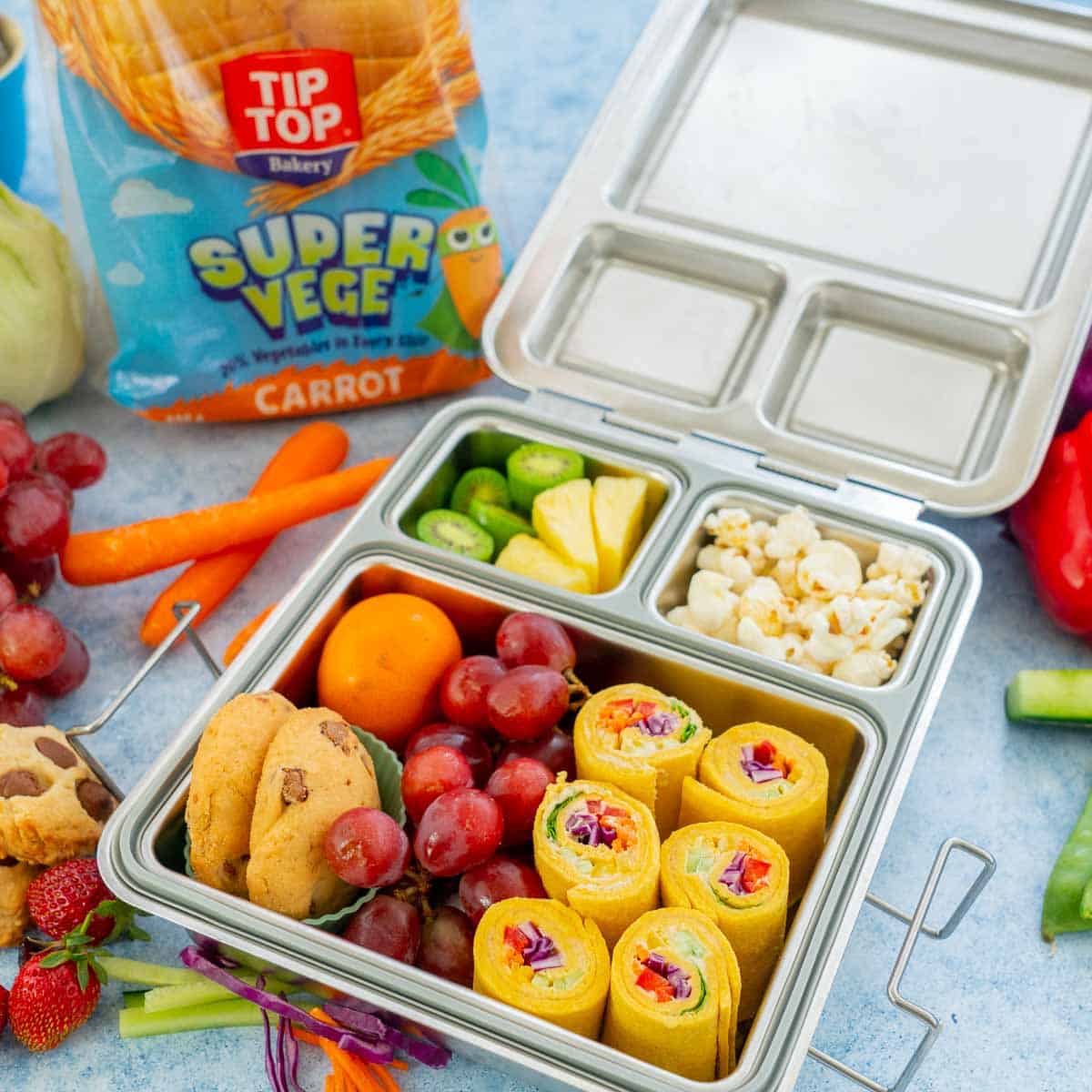 Stainless steel bento lunchbox packed with pinwheel sandwiches, fruit crackers, vegetables and popcorn and chocolate chip cookies.