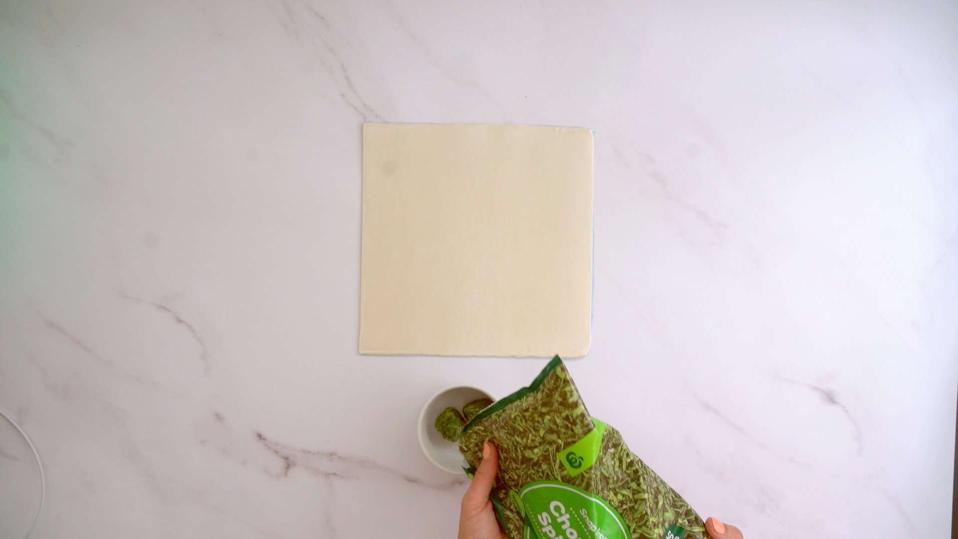A sheet of frozen puff pastry on a marble bench top and a portion of frozen chopped spinach.