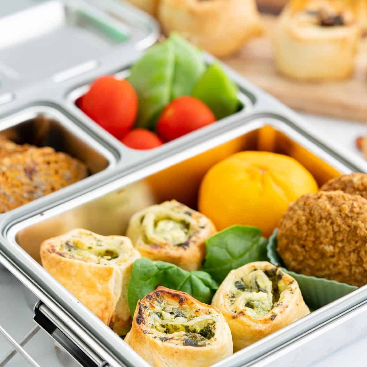 Spinach and feta pinwheels packed in a stainless steel bento lunchbox with colourful produce.