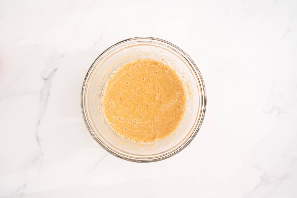 A glass mixing bowl containg beaten wet ingredients.
