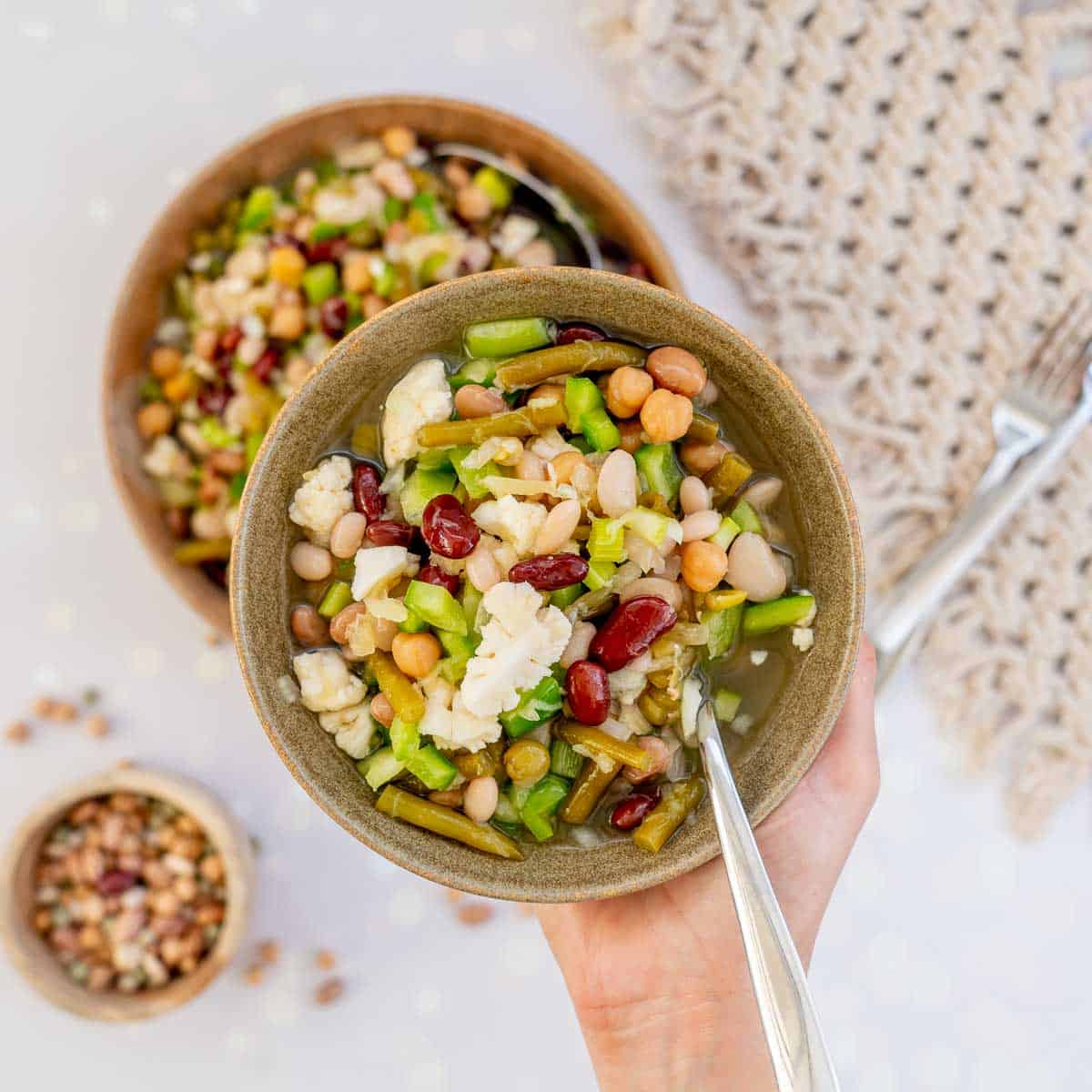 A bowl of bean salad being held above a large salad bowl.