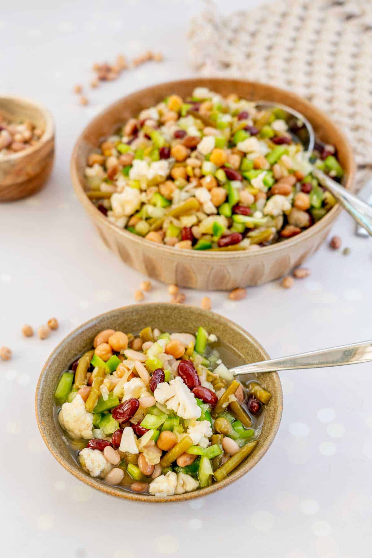 A small bowl of mixed bean salad infront of a large serving dish of bean salad