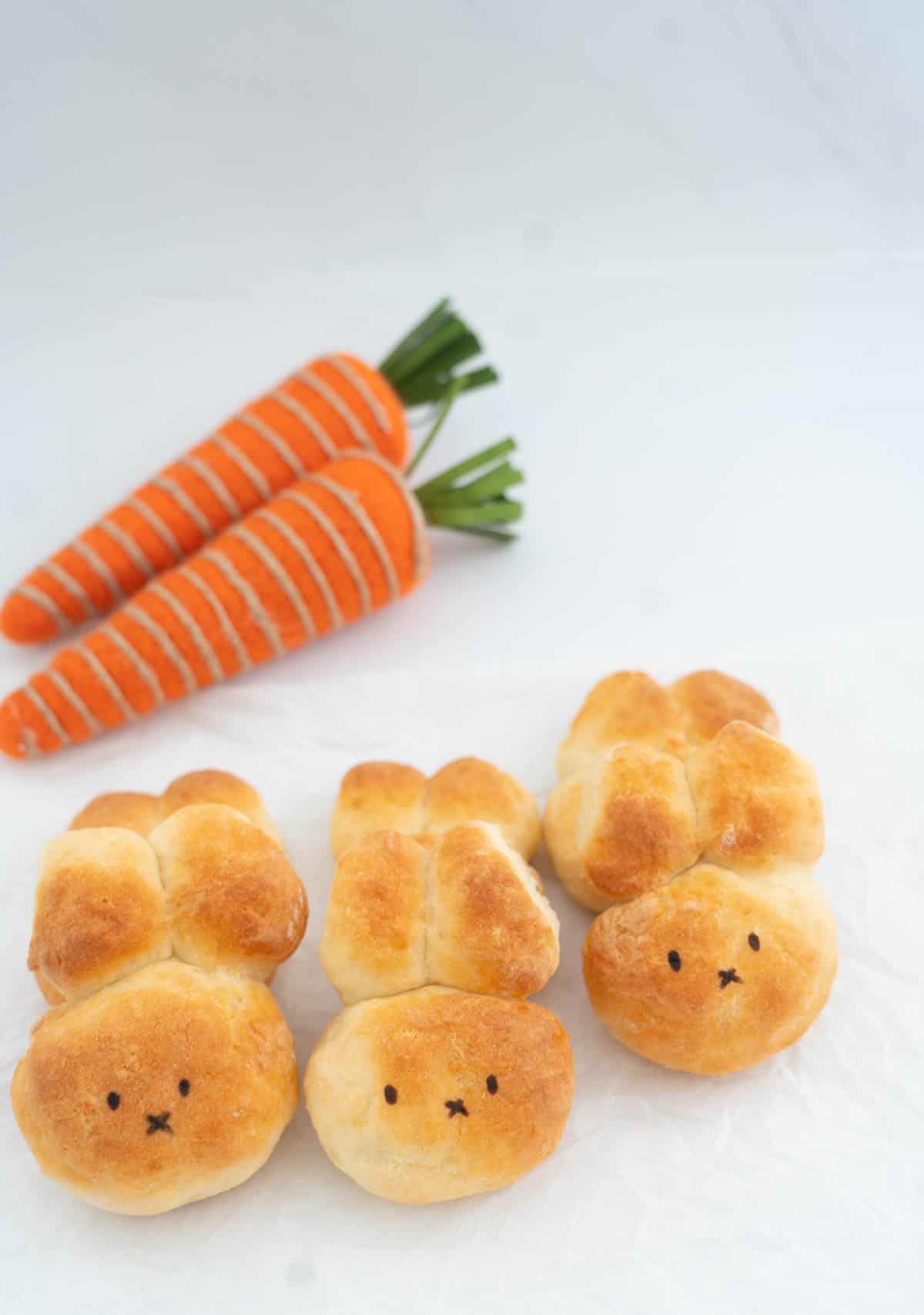 Six bunny buns and 2 felted orange carrots on a white bench top.