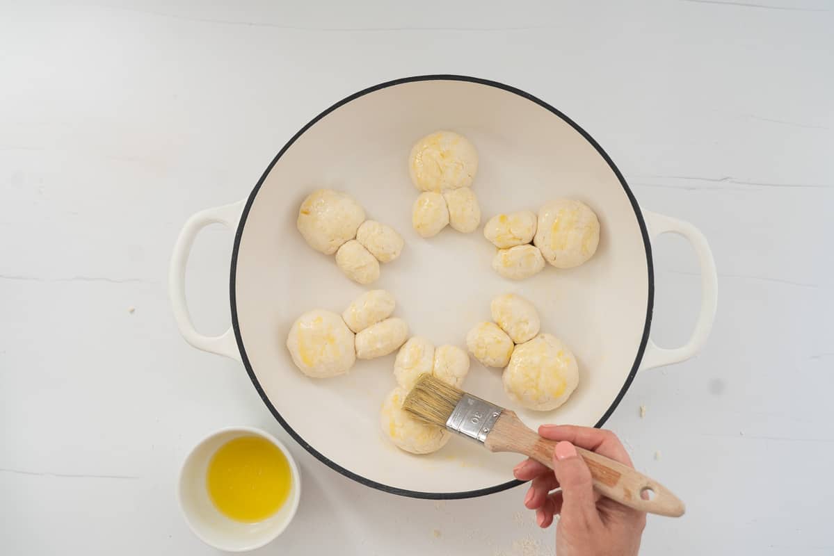 Six bunny buns in a white enamel dish being brushed with melted butter.