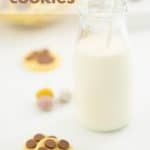 bunny footprint cookies on a white benchtop and a small glass bottle of milk with a straw with text overlay.