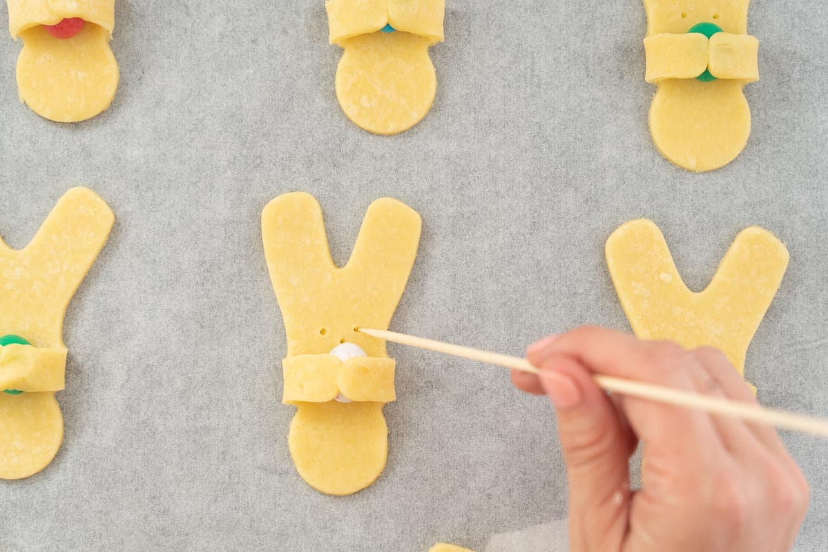 A skewer being used to make wee holes for eyes and nose on an easter bunny cookie.