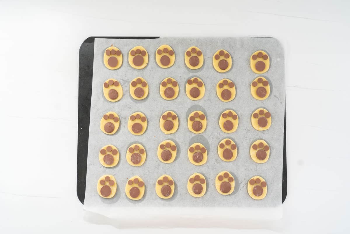 Oval cookies decorated with chocolate buttons and drops to look like bunny footprints, ready to go into the oven.