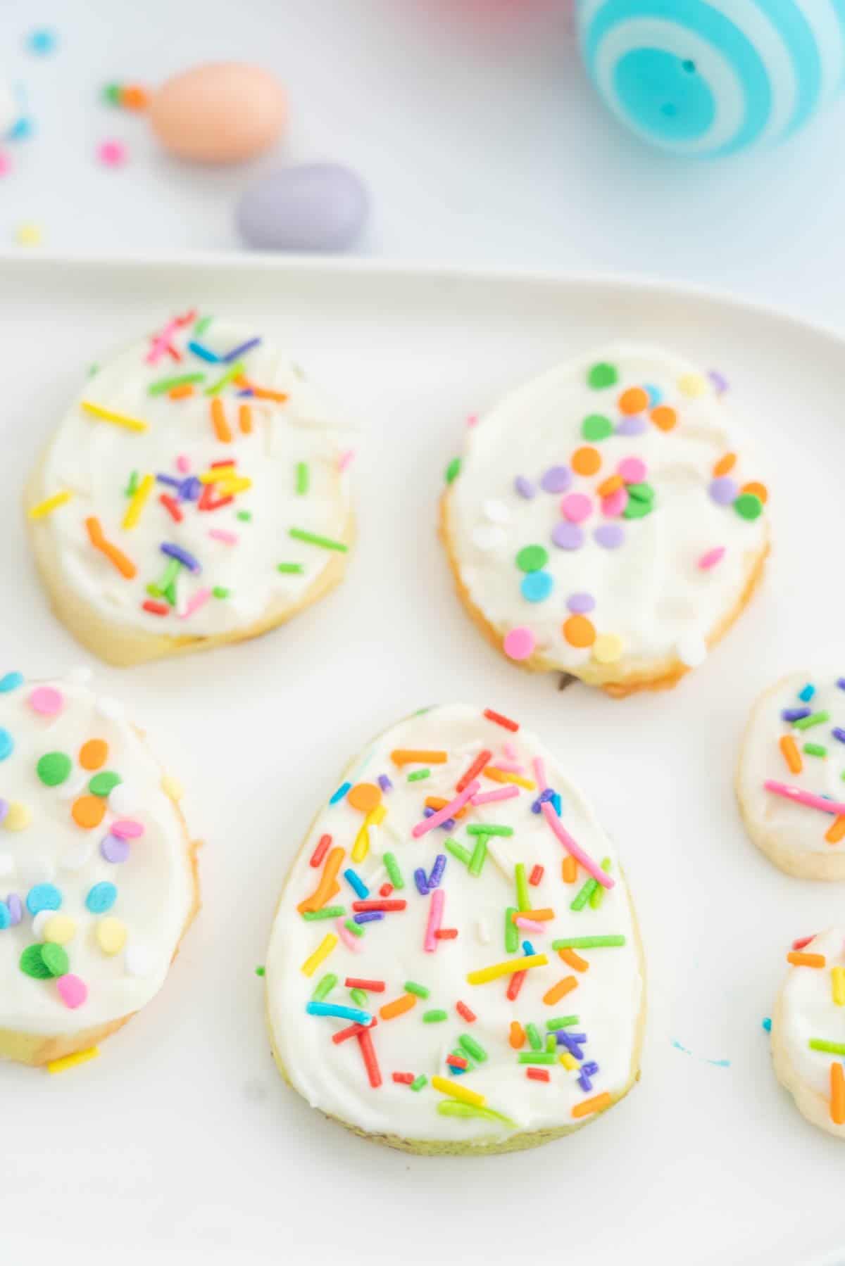 Egg shaped fruit slices, spread with greek yoghurt and toped with sprinkles on a white platter.
