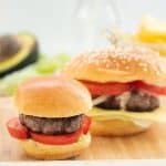 A small and large hamburger sitting on a square bamboo plate.