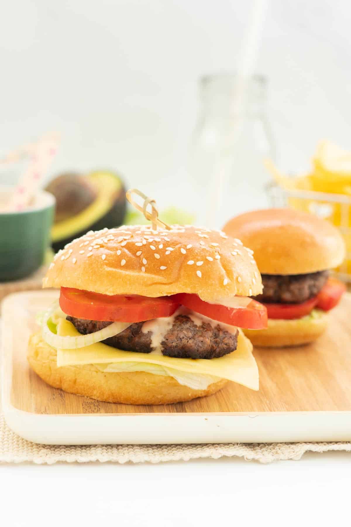 A small and large hamburger sitting on a square bamboo plate.