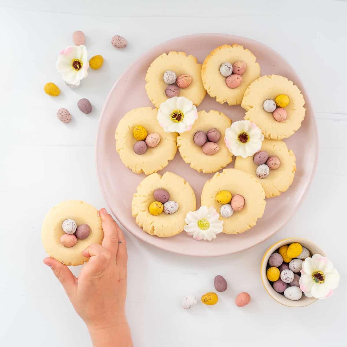 A child's hand reaching for a mini egg cookie.