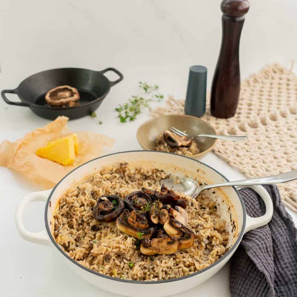 A large dish filled with mushroom risotto, topped with sliced mushrooms and garnished with thyme leaves.