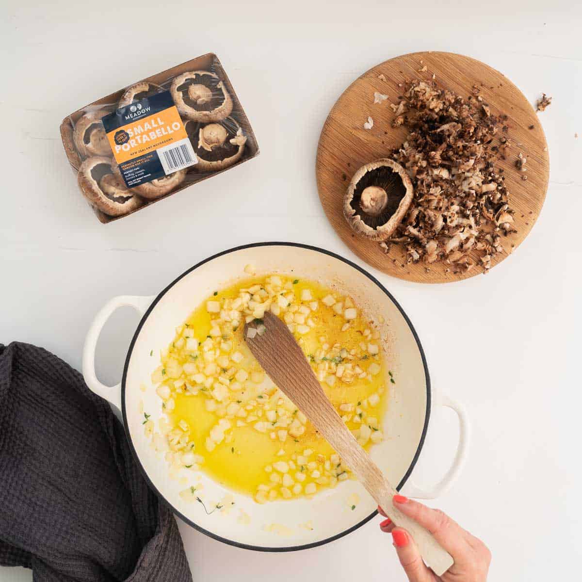 A chopping board of grated mushrooms and a white ceramic pan of oil and onion.