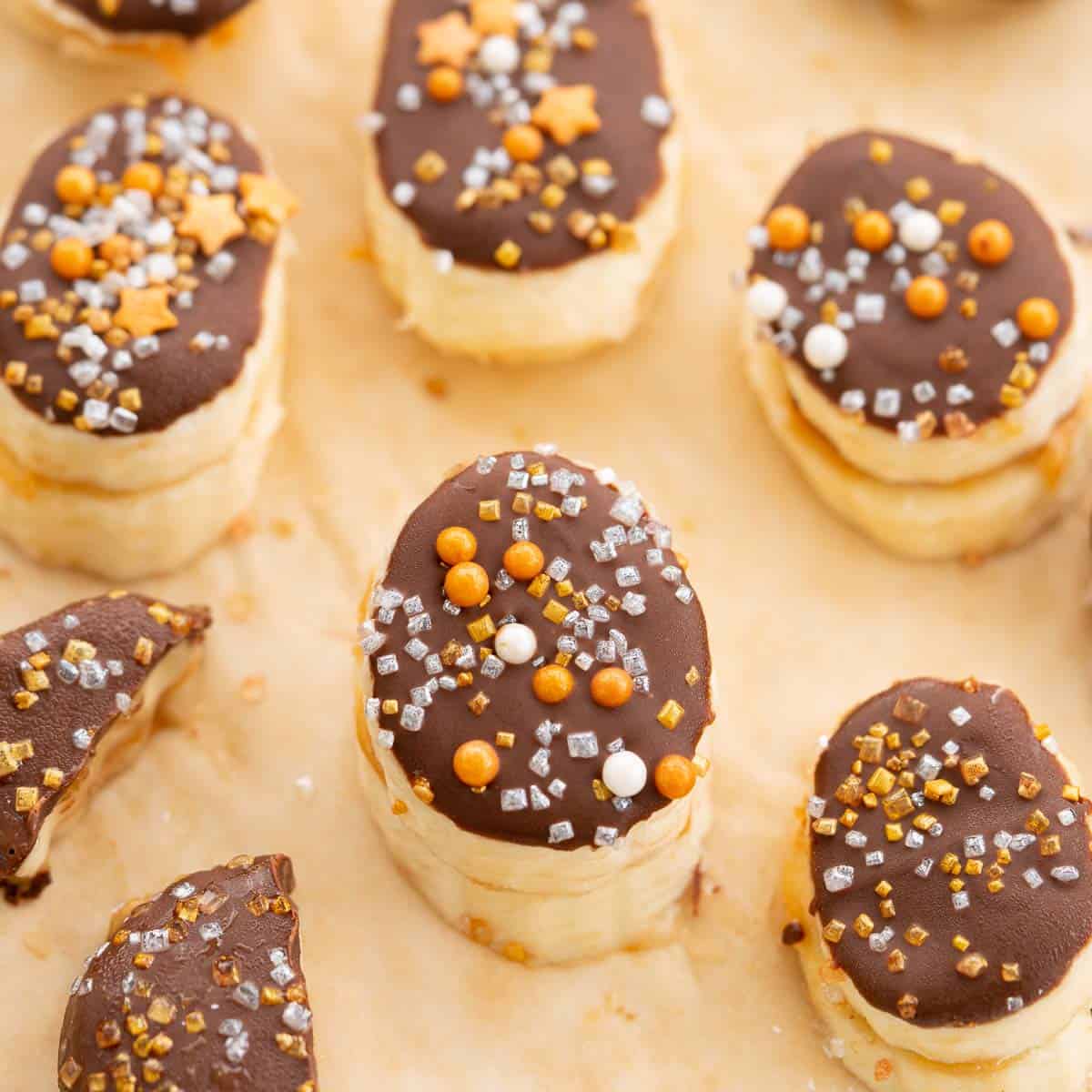 Frozen banana slices covered in chocolate and decorated with gold and silver sprinkles.