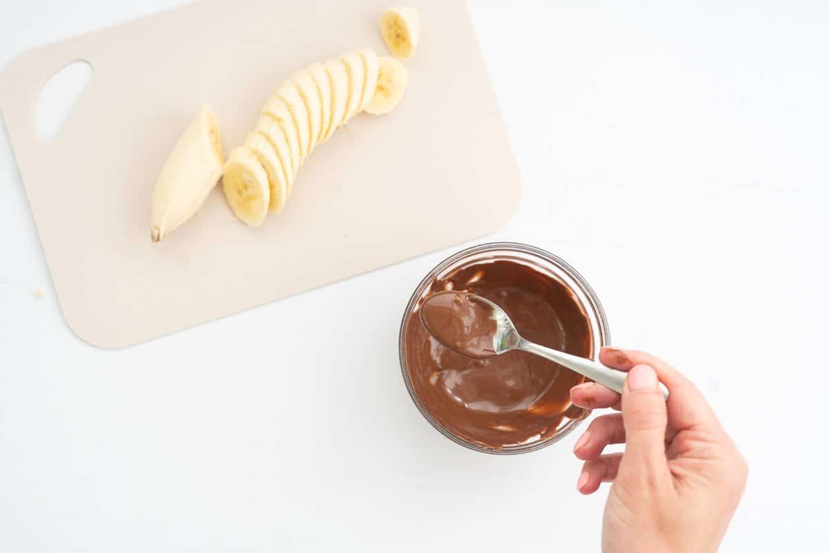 A small glass bowl of melted chocolate being stirred with a teaspoon.